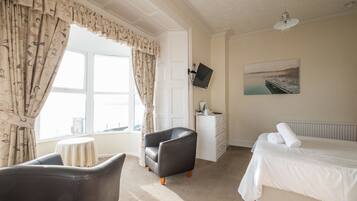 A hotel room with a bed, a chair, a desk, a TV, and a window with curtains.