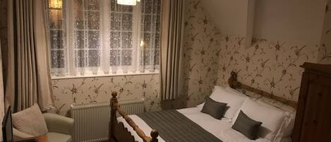 A bedroom with a wooden bed, a chair, a radiator, and a window with curtains.