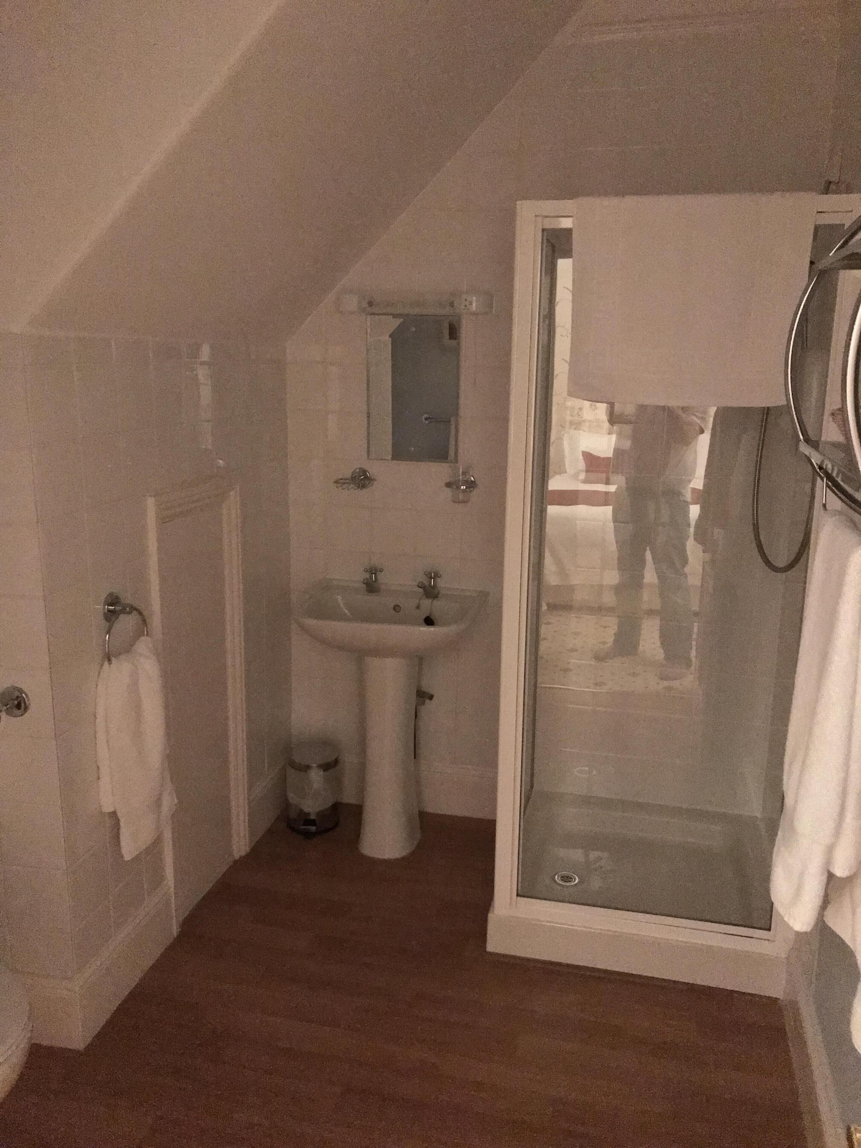 A small, dimly lit bathroom with a shower, sink, and a mirror above the sink.