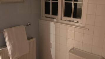 A bathroom with a toilet, a radiator, and a window with a blue valance.
