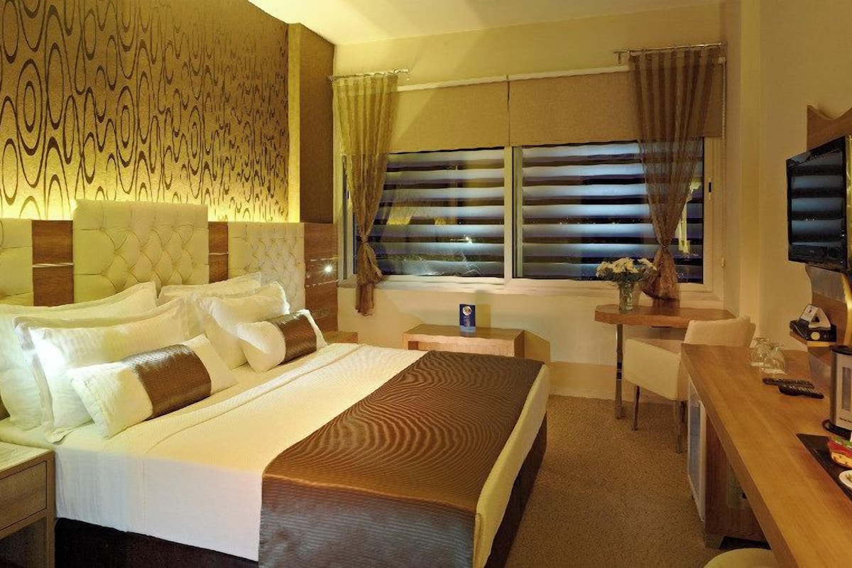 Een hotelkamer met een groot bed, een bureau, een televisie en een raam met gordijnen.