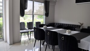 Un comedor moderno con una mesa larga, sillas negras y vistas a la vegetación exterior.