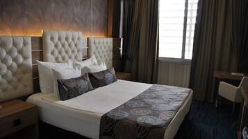 A hotel room with a large bed, a wooden nightstand, a desk, and a window with curtains.