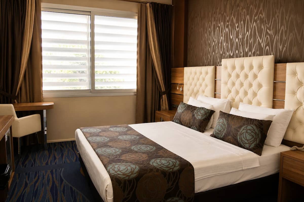 Een hotelkamer met een groot bed, een bureau en een raam met gordijnen.