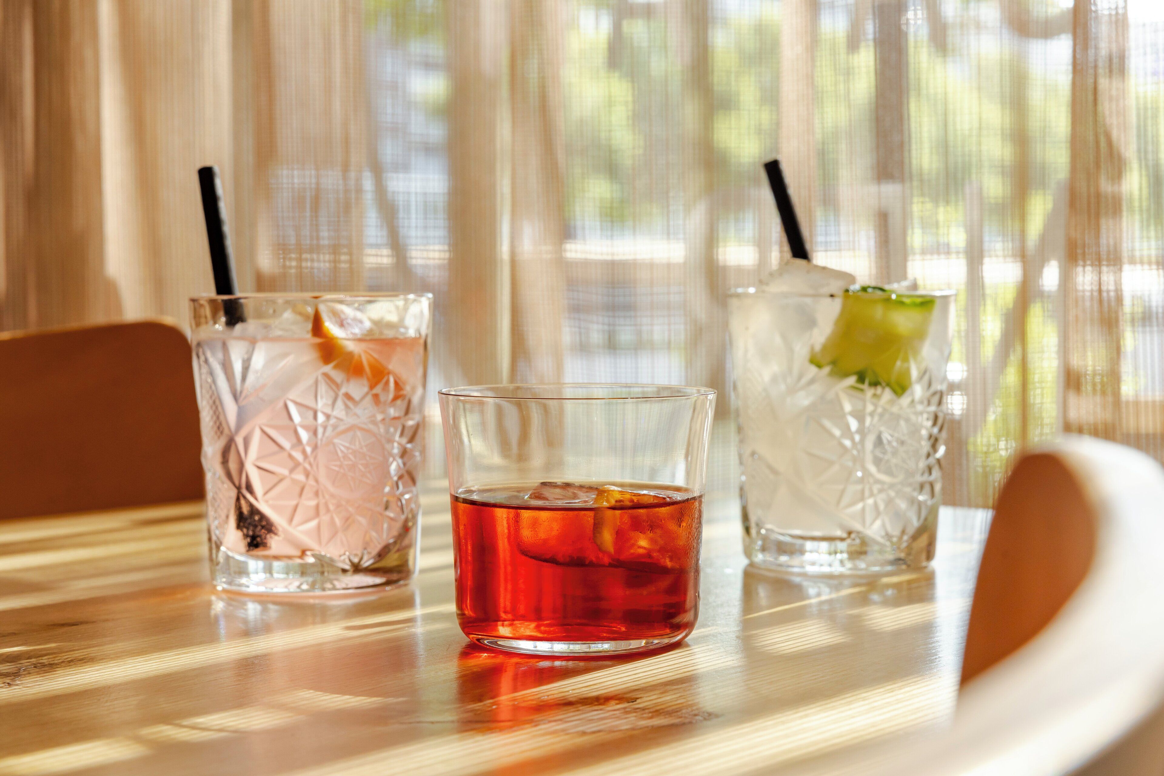 Three glasses of beverages on a table with a view of a window with sheer curtains.