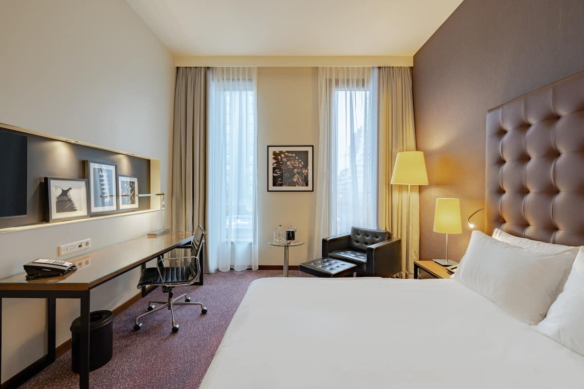 Une chambre d’hôtel avec un grand lit, un bureau avec une chaise, une télévision et une petite table avec une lampe.