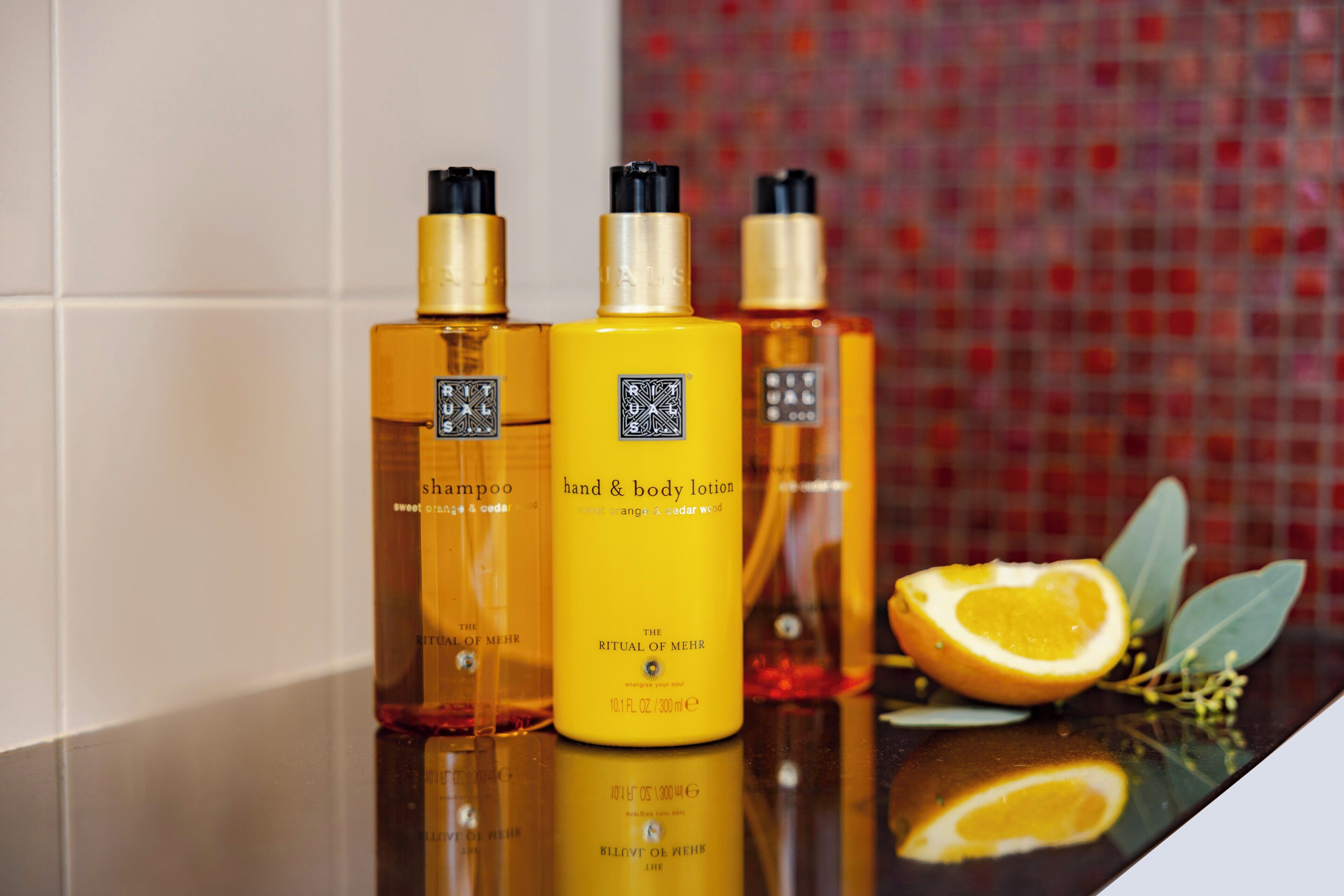 Trois flacons de lotion pour les mains et le corps de la gamme Ritual of Mehr, placés sur une surface réfléchissante.