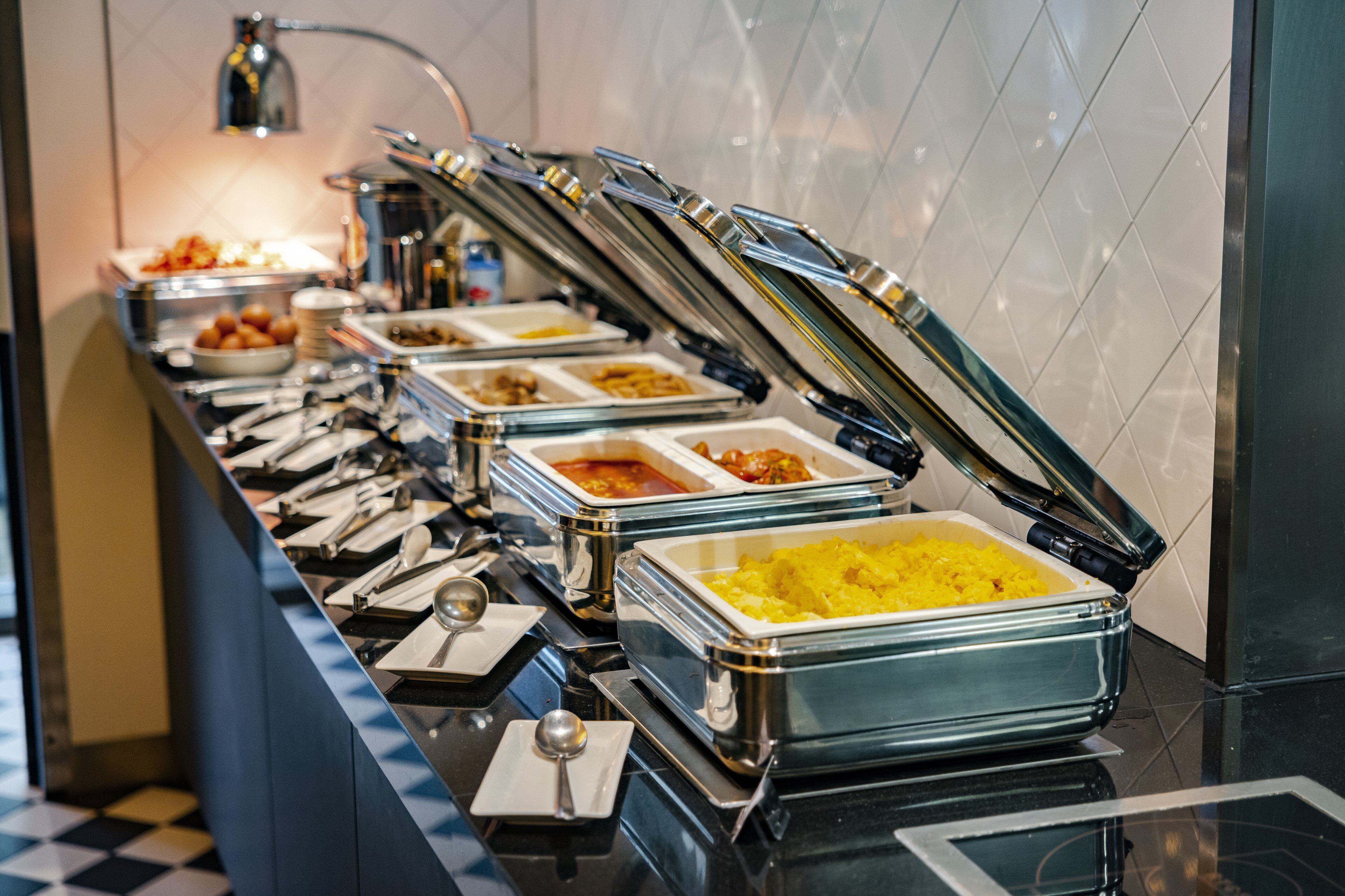 A buffet line with various food options, including a large container of yellow rice, several dishes of curry, and other prepared meals.