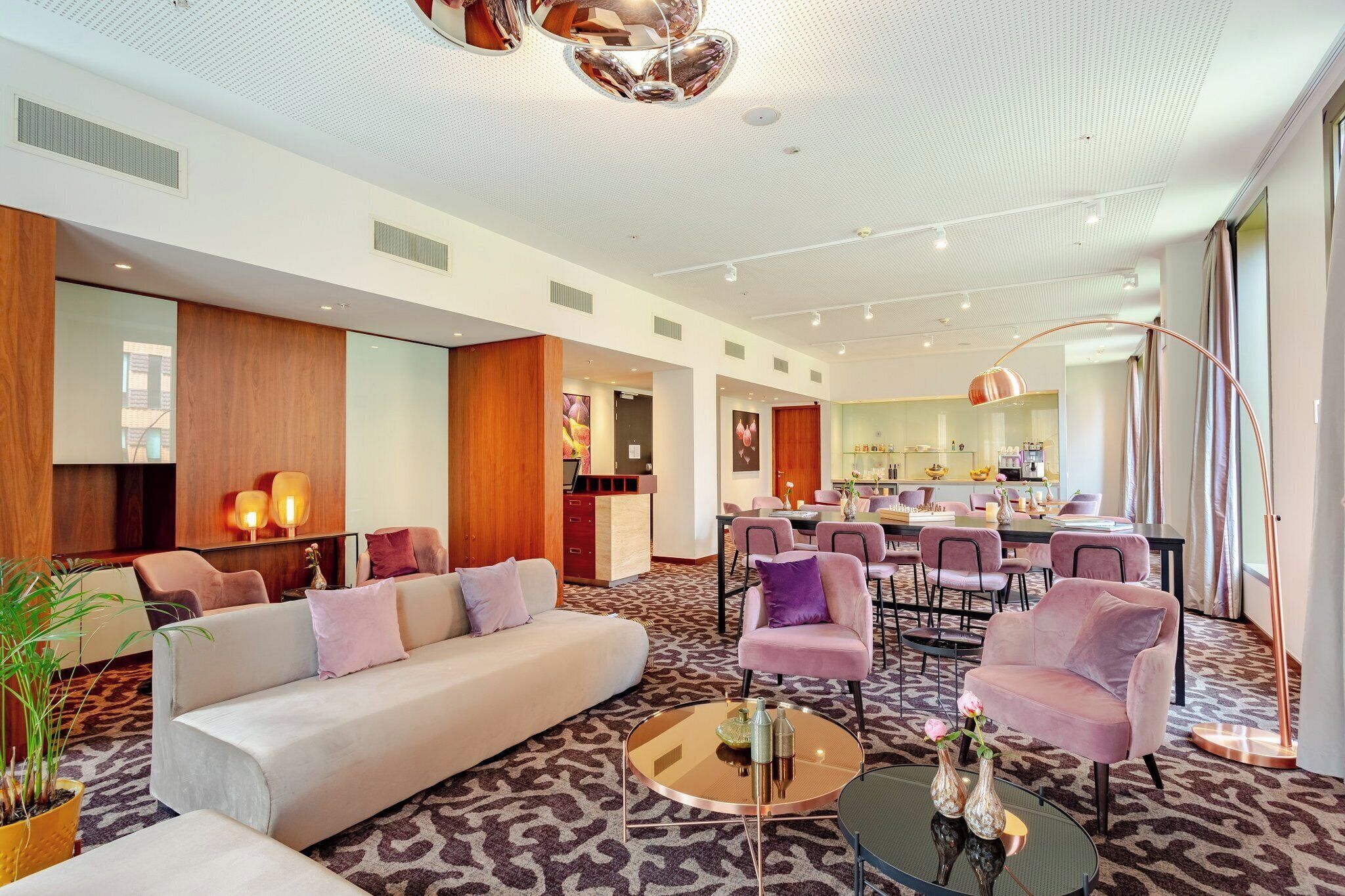 Eine moderne Hotelhalle mit einer Couch, Sesseln, einem Couchtisch und einer Küchenzeile im Hintergrund.