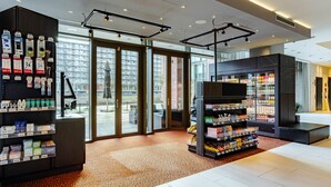A modern hotel lobby with a large glass door leading to an outdoor area, a self-service beverage station, and a variety of toiletries on shelves. - Crowne Plaza Amsterdam South by IHG (Amsterdam)