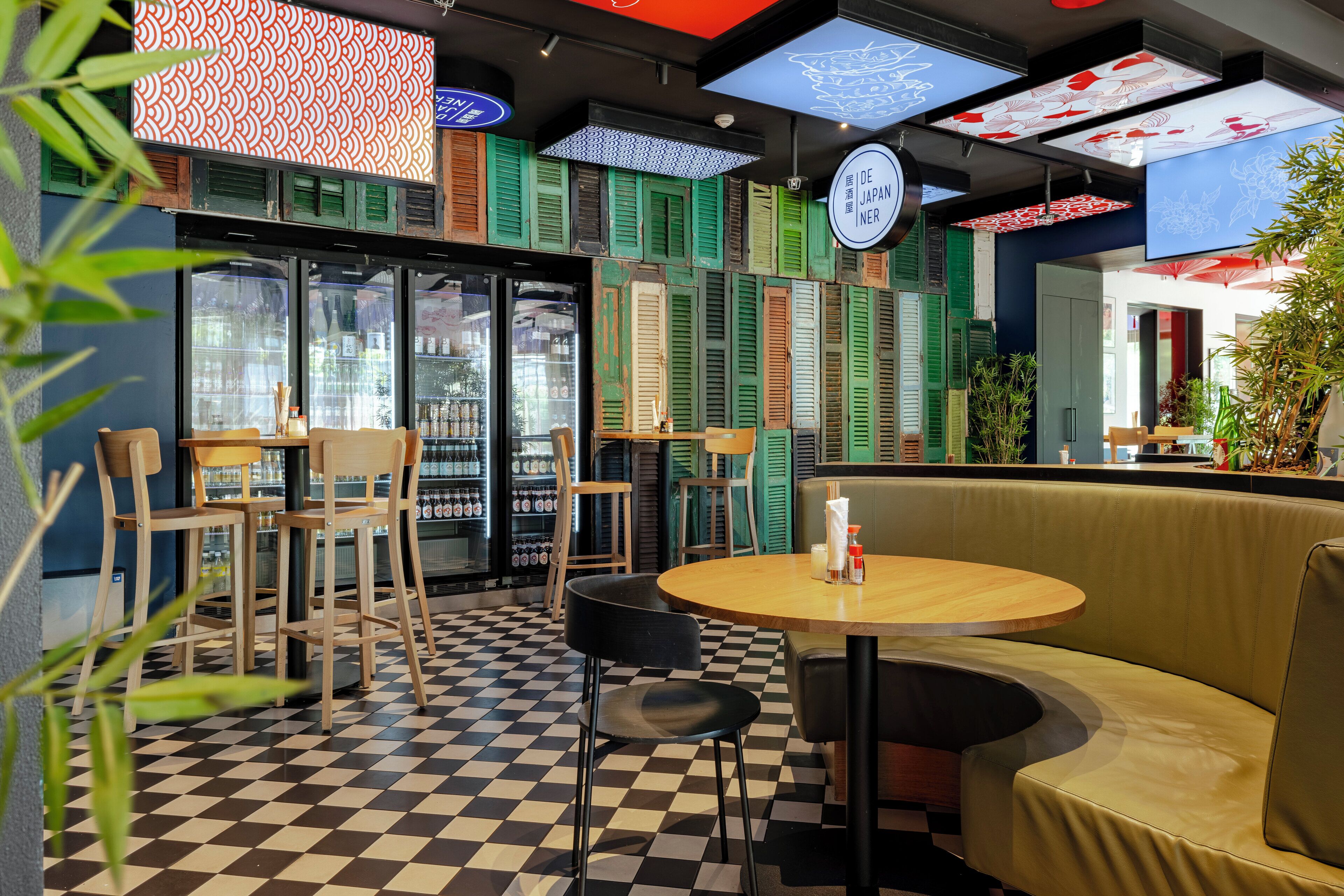 A restaurant interior with checkered flooring, wooden tables, and green shutters on the walls.