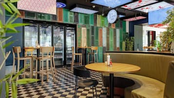 Interior de un restaurante con suelo a cuadros, mesas de madera y contraventanas verdes en las paredes.