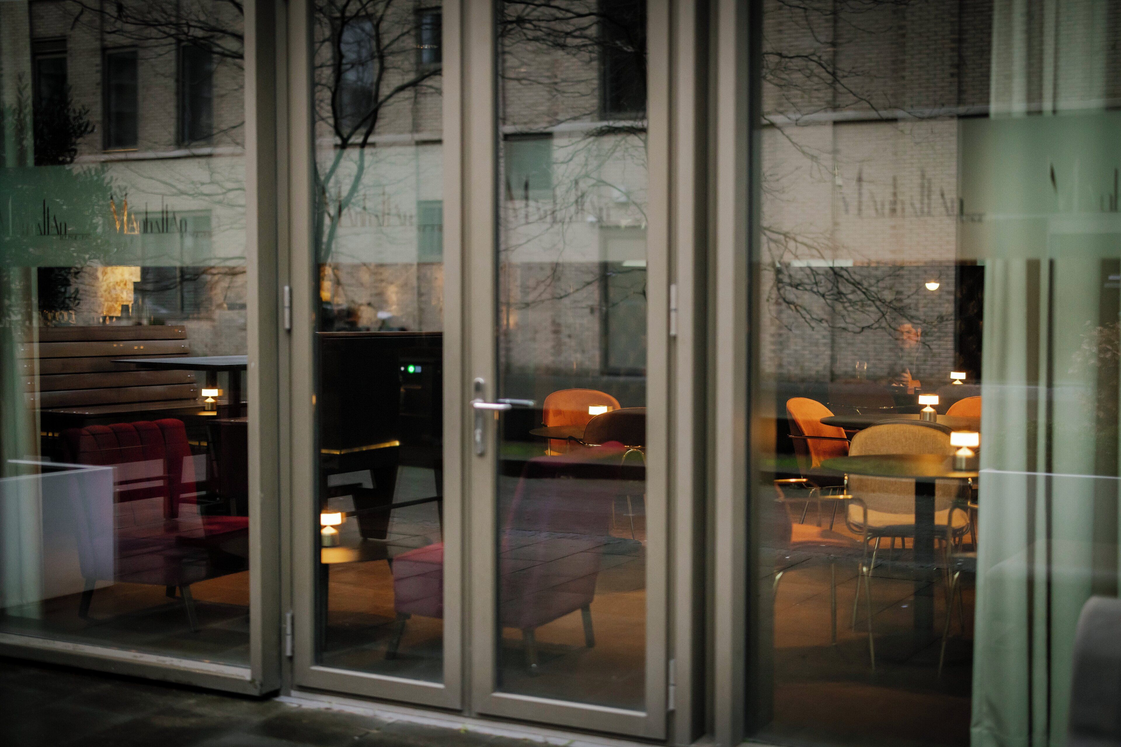 A restaurant with glass doors, interior seating, and tables with candles.