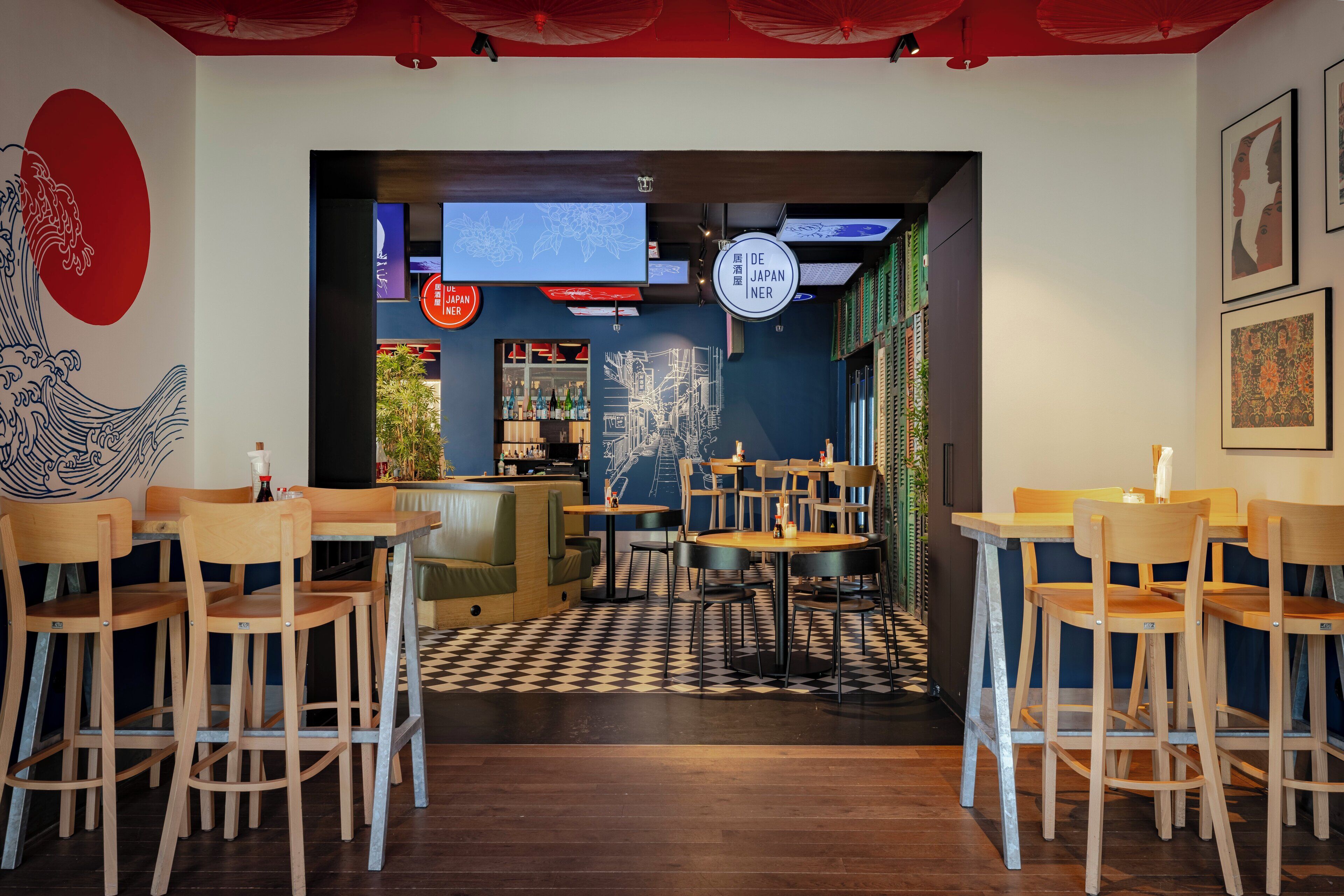 Interior de restaurante con mesas y sillas de madera, suelo a cuadros y una pared con diseño de olas japonesas.