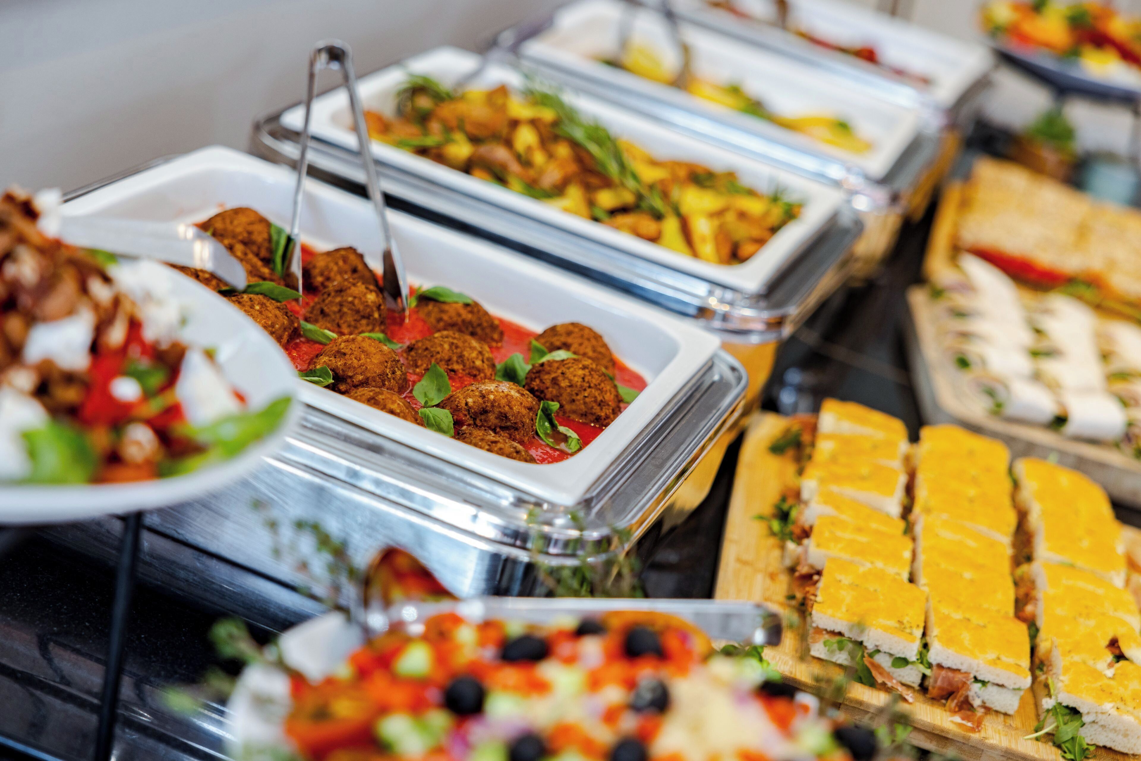 Buffet com diversas opções de comida, incluindo almôndegas, saladas e sanduíches.