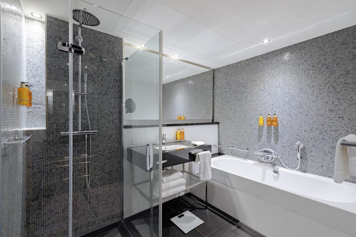 Une salle de bain moderne avec une douche à parois de verre, une baignoire blanche et un mur recouvert de carreaux.