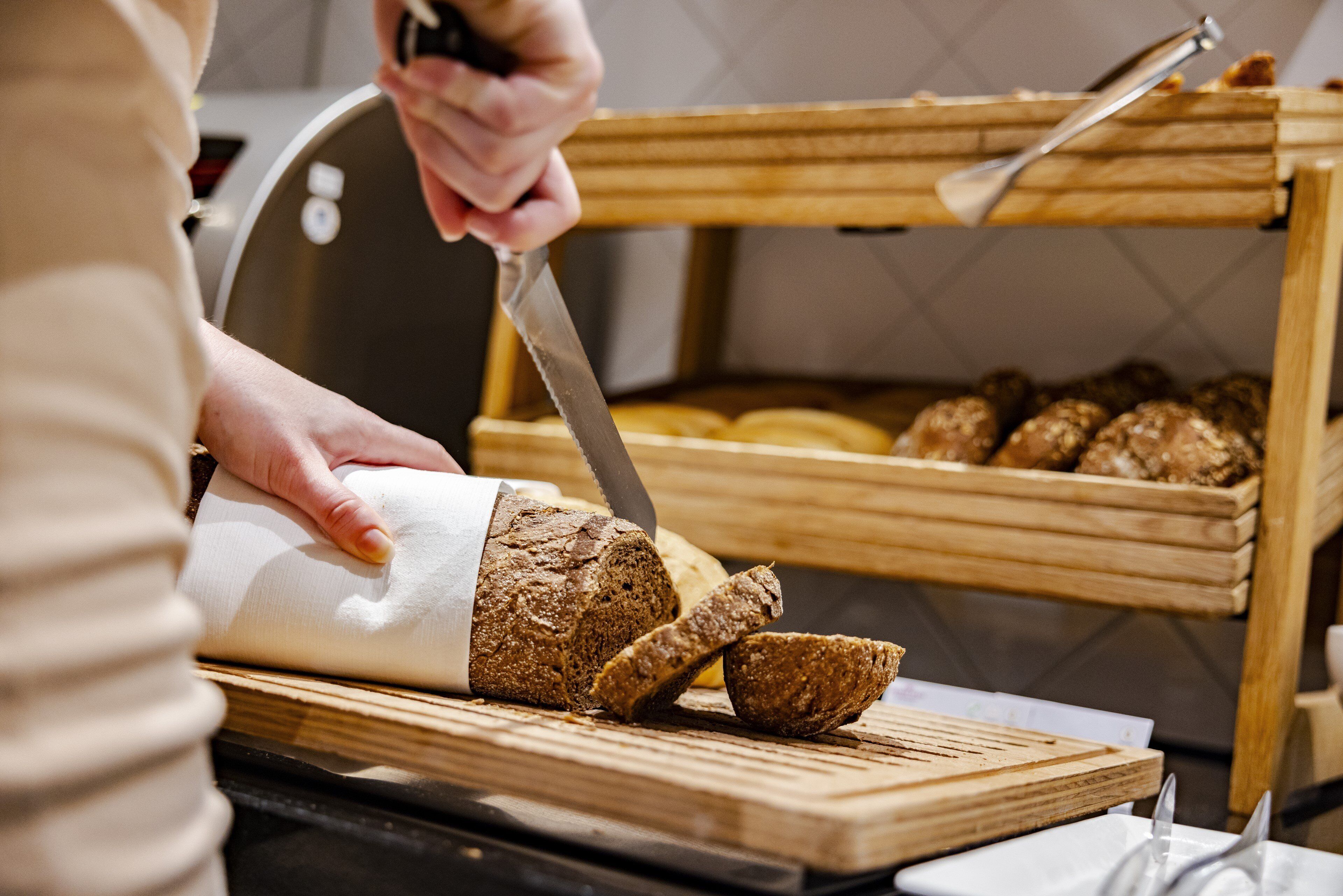A person slicing bread on a wooden cutting board.