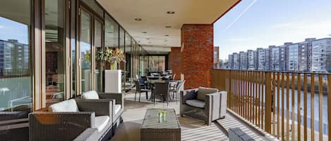 A balcony with wicker furniture, a table with flowers, and a view of buildings and a river.
