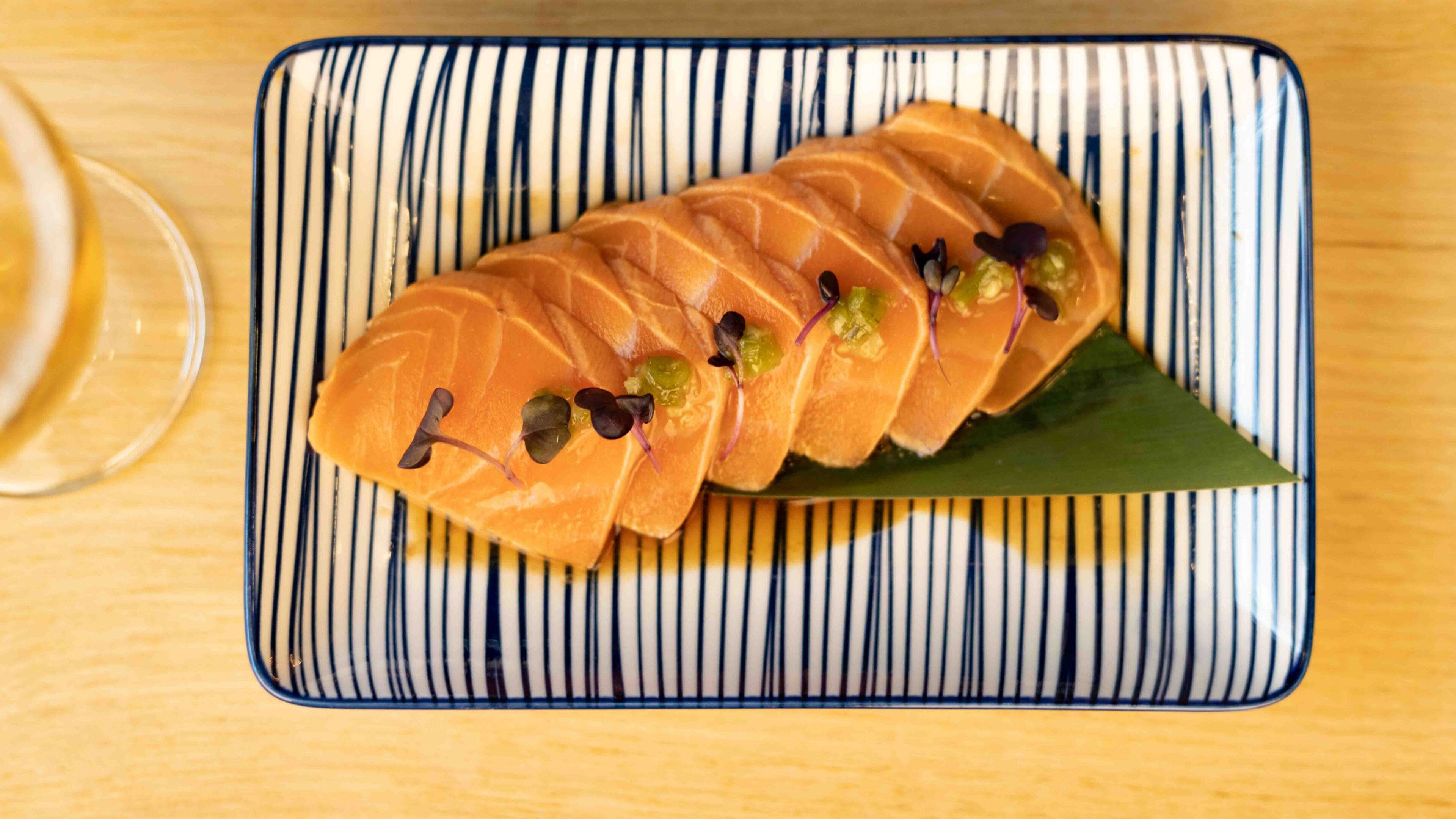 A sushi dish with salmon slices on a striped plate.