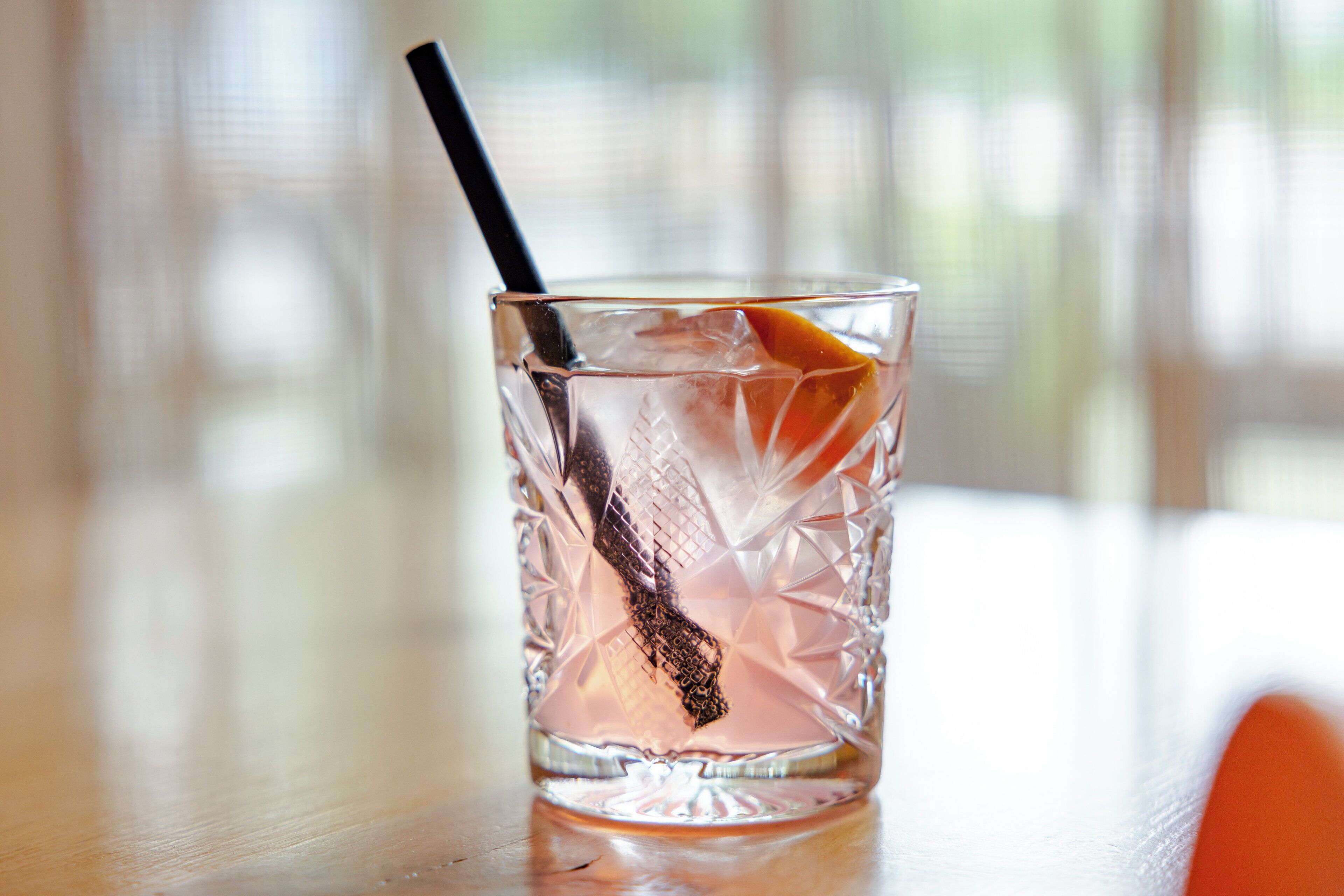 A clear glass with a black straw and an orange slice, placed on a wooden surface.