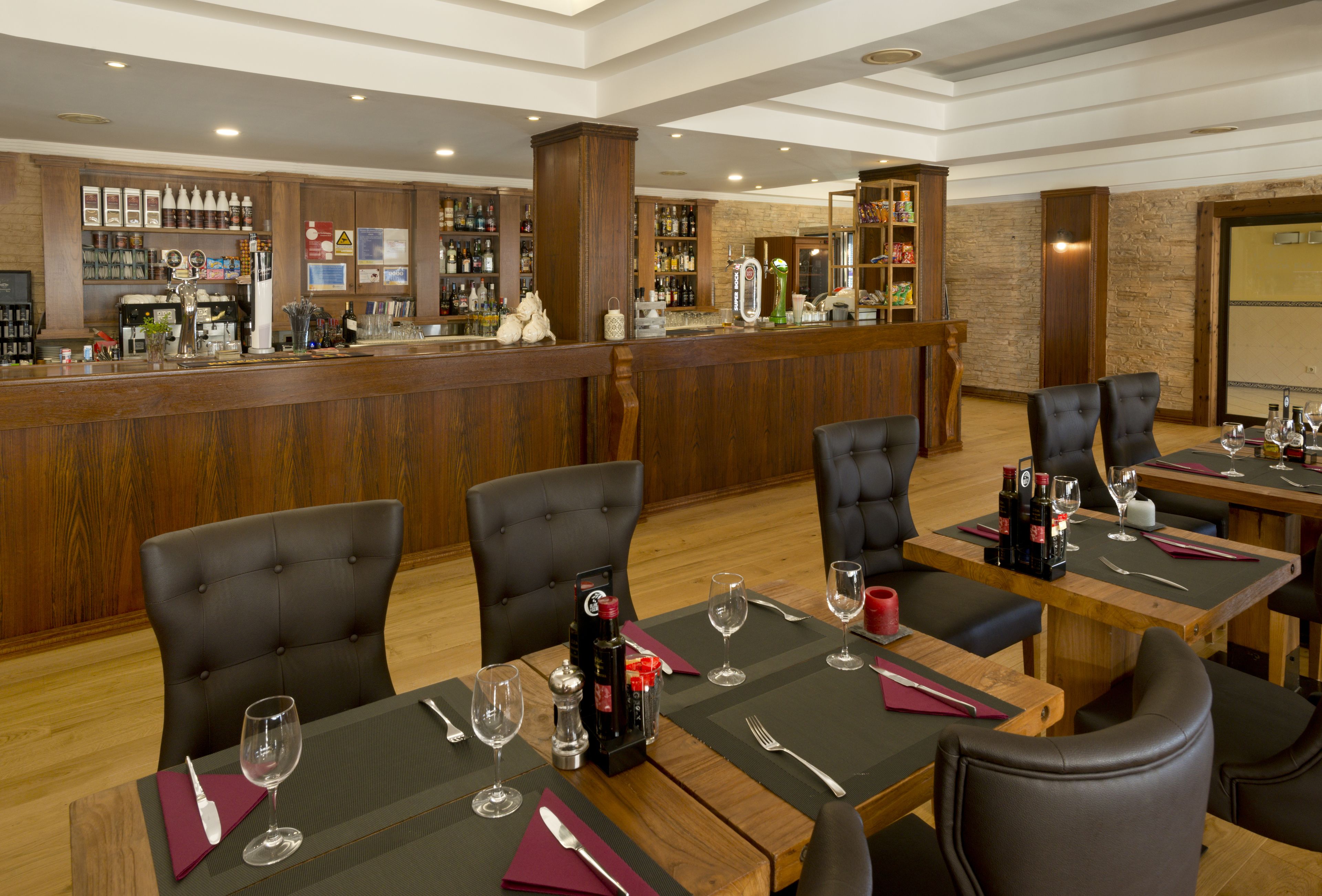 Un restaurante con mesas de madera, sillas de cuero negro y una zona de bar con varias botellas y copas.