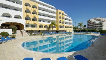 A hotel with a swimming pool, multiple balconies, and sun loungers.