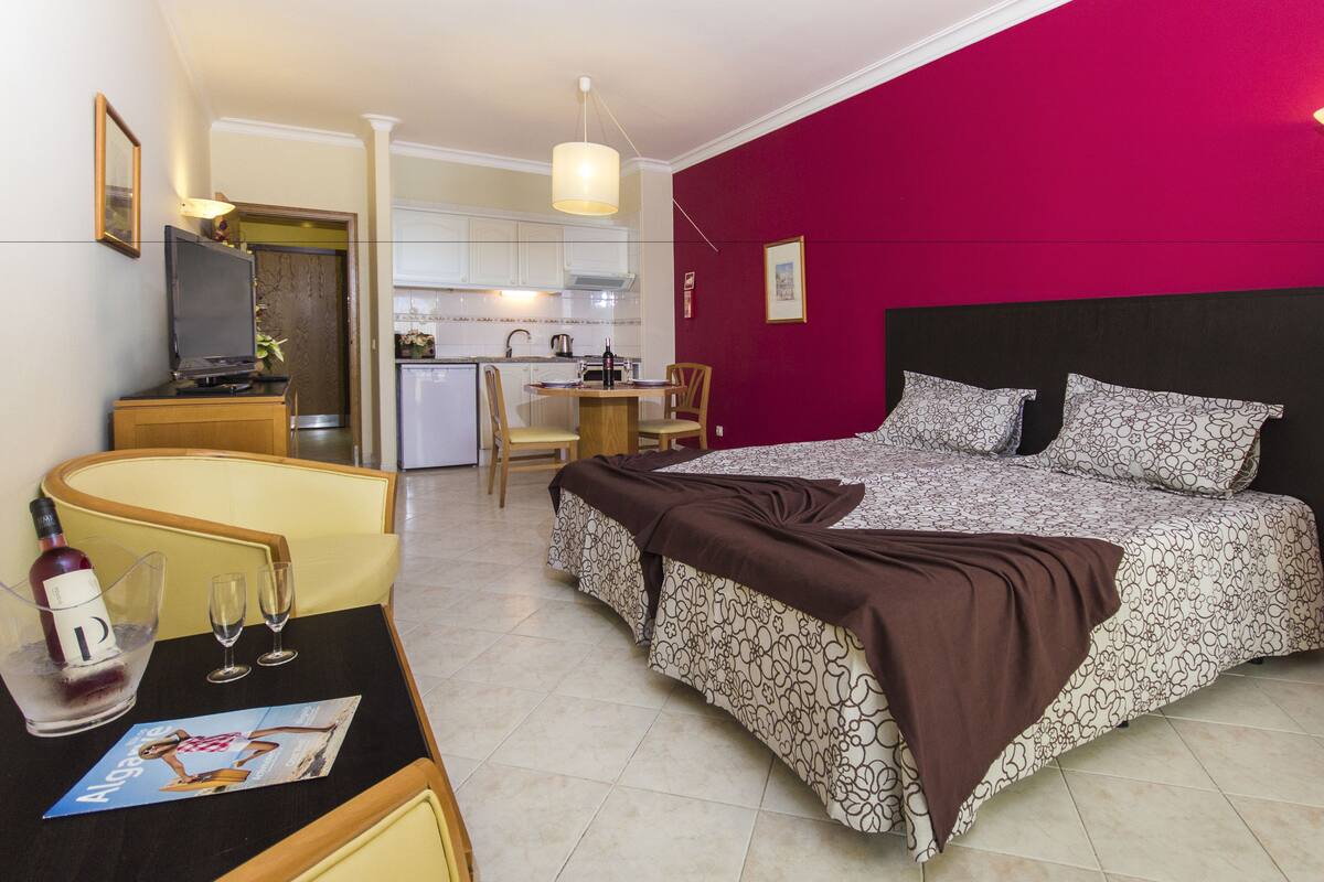 Una habitación de hotel con cama, escritorio con silla, kitchenette pequeña y zona de comedor.