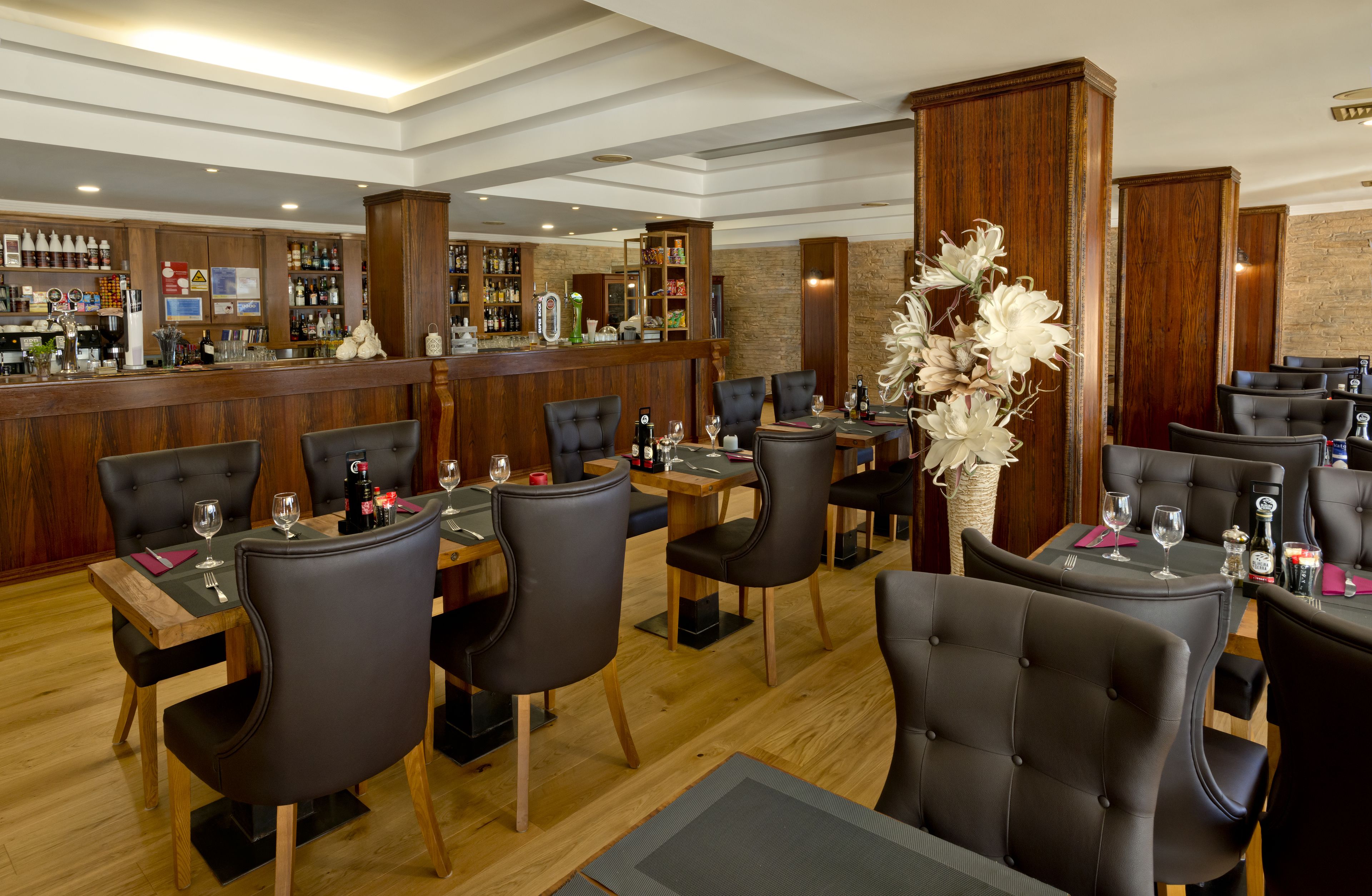 A restaurant with wooden bar and booths, tables with chairs, and a decorative vase.