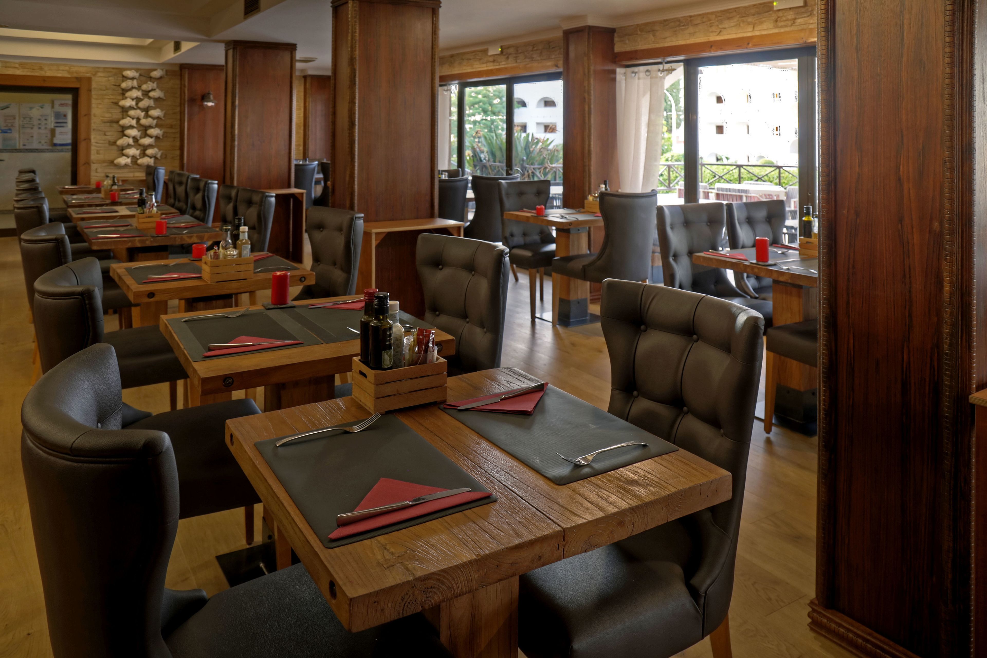 A restaurant with multiple tables and booths, wooden flooring, and large windows with a view of the outdoors.