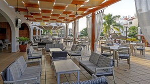 An outdoor cafe with multiple seating areas, including sofas and tables, under a covered roof with wooden beams and hanging lights. - Paladim & Alagoamar Hotels (Albufeira)