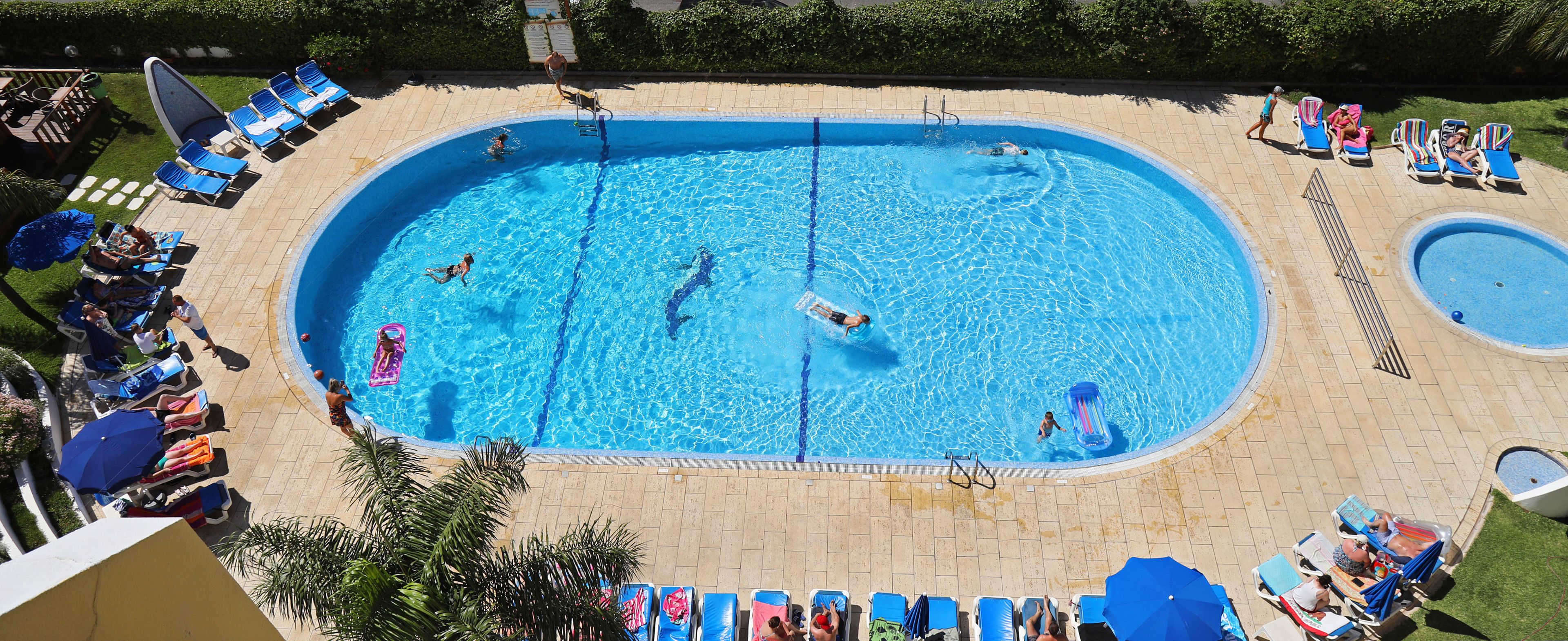 A large rectangular swimming pool surrounded by lounge chairs and umbrellas, with a smaller circular pool to the right.