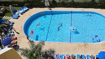 A large rectangular swimming pool surrounded by lounge chairs and umbrellas, with a smaller circular pool to the right.