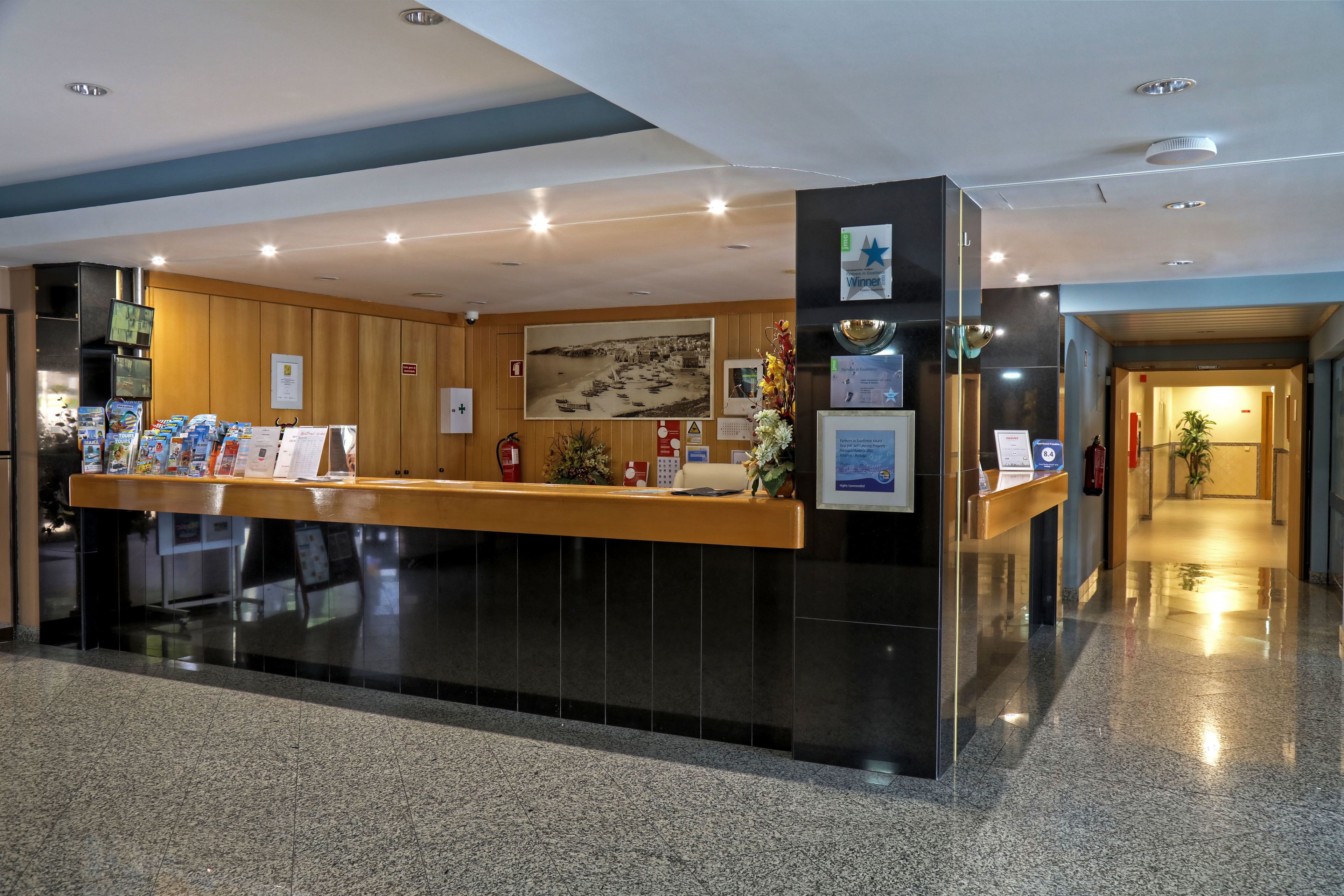 A reception area with a counter, informational posters, a fire extinguisher, and a corridor leading to other areas.