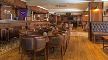 A bar area with wooden furniture, a bar counter, and a seating area with cushioned chairs and a sofa.