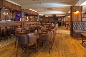 Una zona de bar con mobiliario de madera, una barra y un área de estar con sillas acolchadas y un sofá.