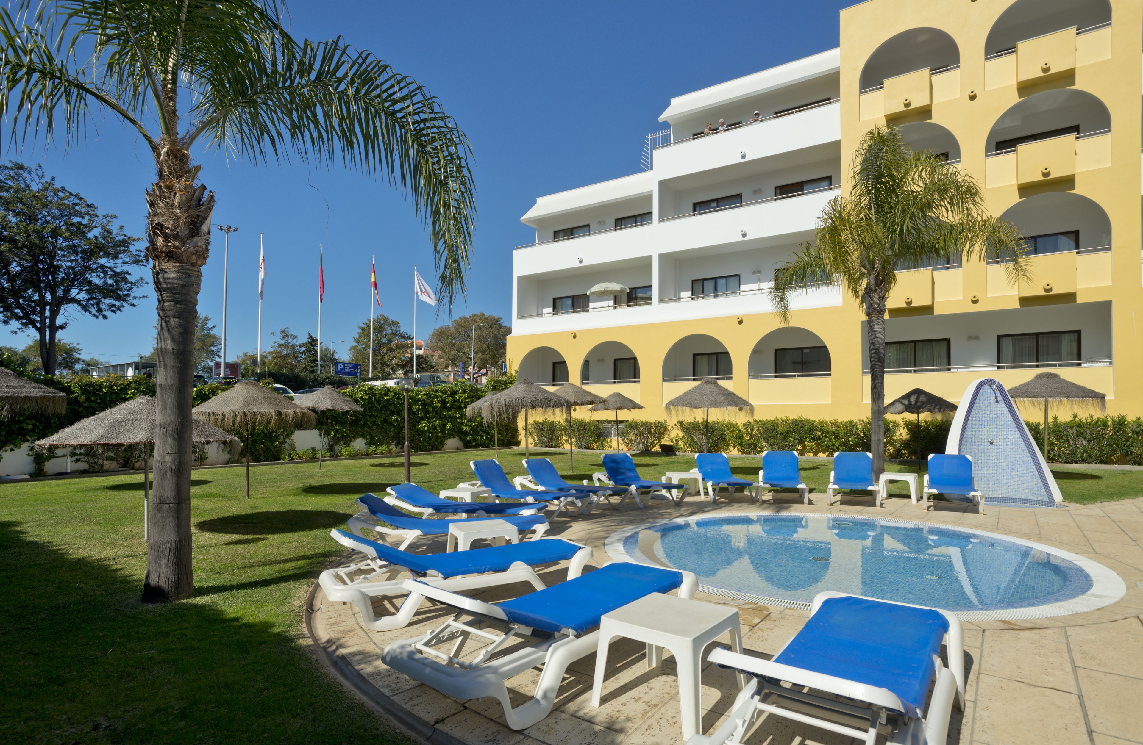 A hotel with a swimming pool, lounge chairs, and palm trees.