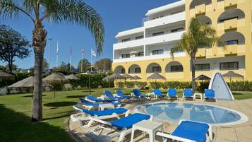 A hotel with a swimming pool, lounge chairs, and palm trees.