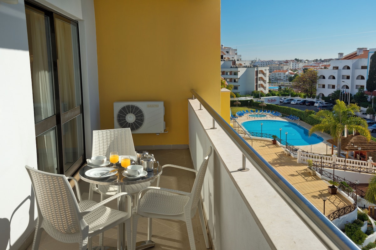 Ein Balkon mit Esstisch und Stühlen, ein Schwimmbad und Blick auf die umliegenden Gebäude.