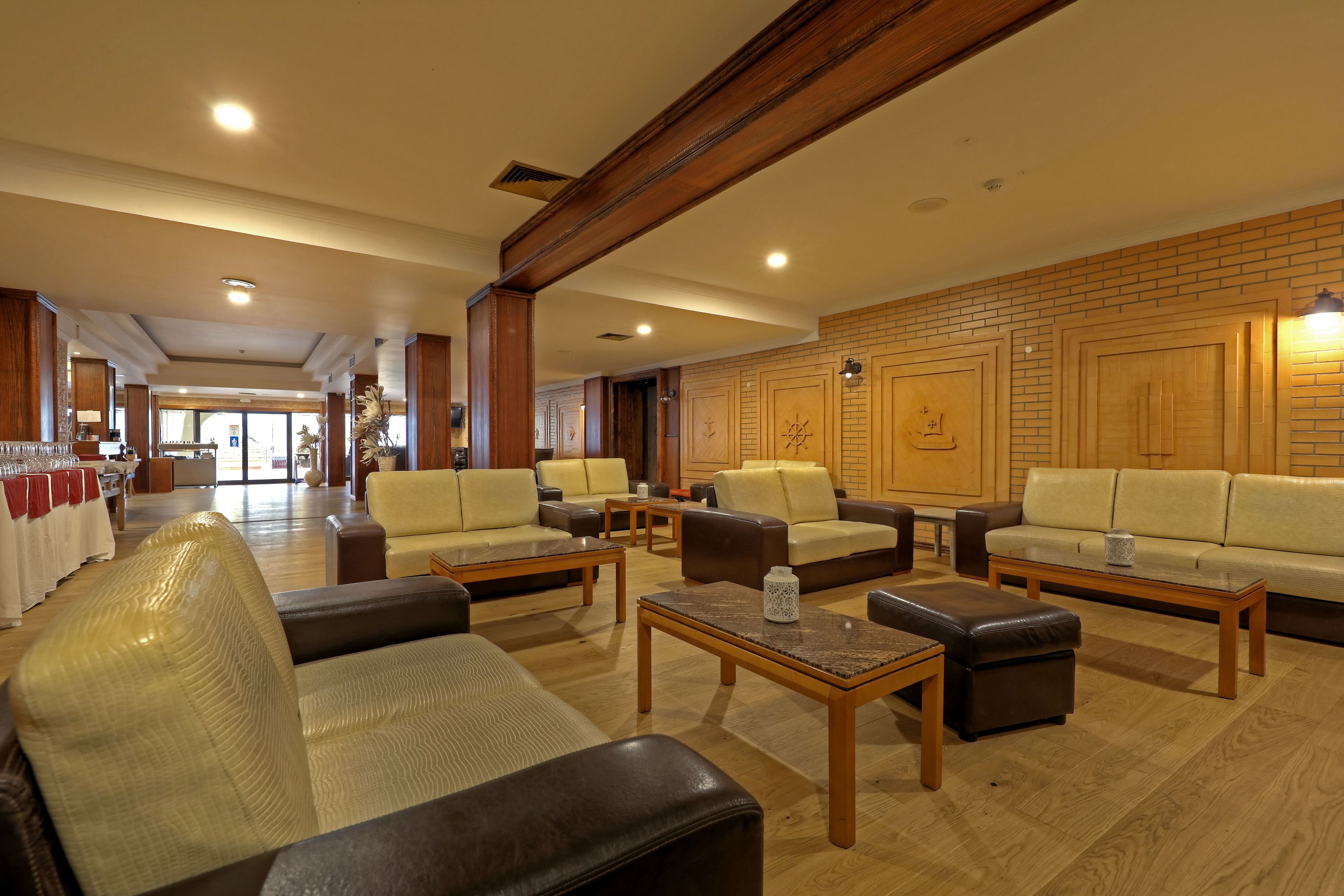 A spacious lobby with leather sofas, wooden tables, and a brick wall with decorative panels.