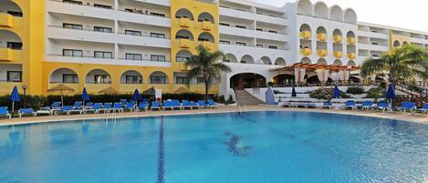 Un hôtel doté d’une grande piscine, de nombreux balcons et de chaises longues bleues.