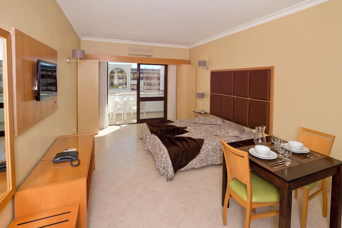 Habitación de hotel con cama, escritorio con teléfono, mesa de comedor para dos personas y vistas al balcón exterior.