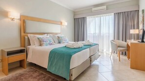 Une chambre d’hôtel comprenant un lit, des tables de chevet, un bureau, une chaise, une télévision et une fenêtre avec des rideaux.