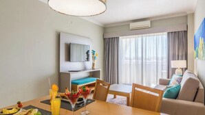 Une chambre d’hôtel équipée d’une table à manger, de chaises, d’un canapé, d’une télévision et d’une fenêtre avec des rideaux.