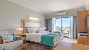 Une chambre d’hôtel avec un lit, un bureau, une chaise, une télévision et un balcon avec vue.