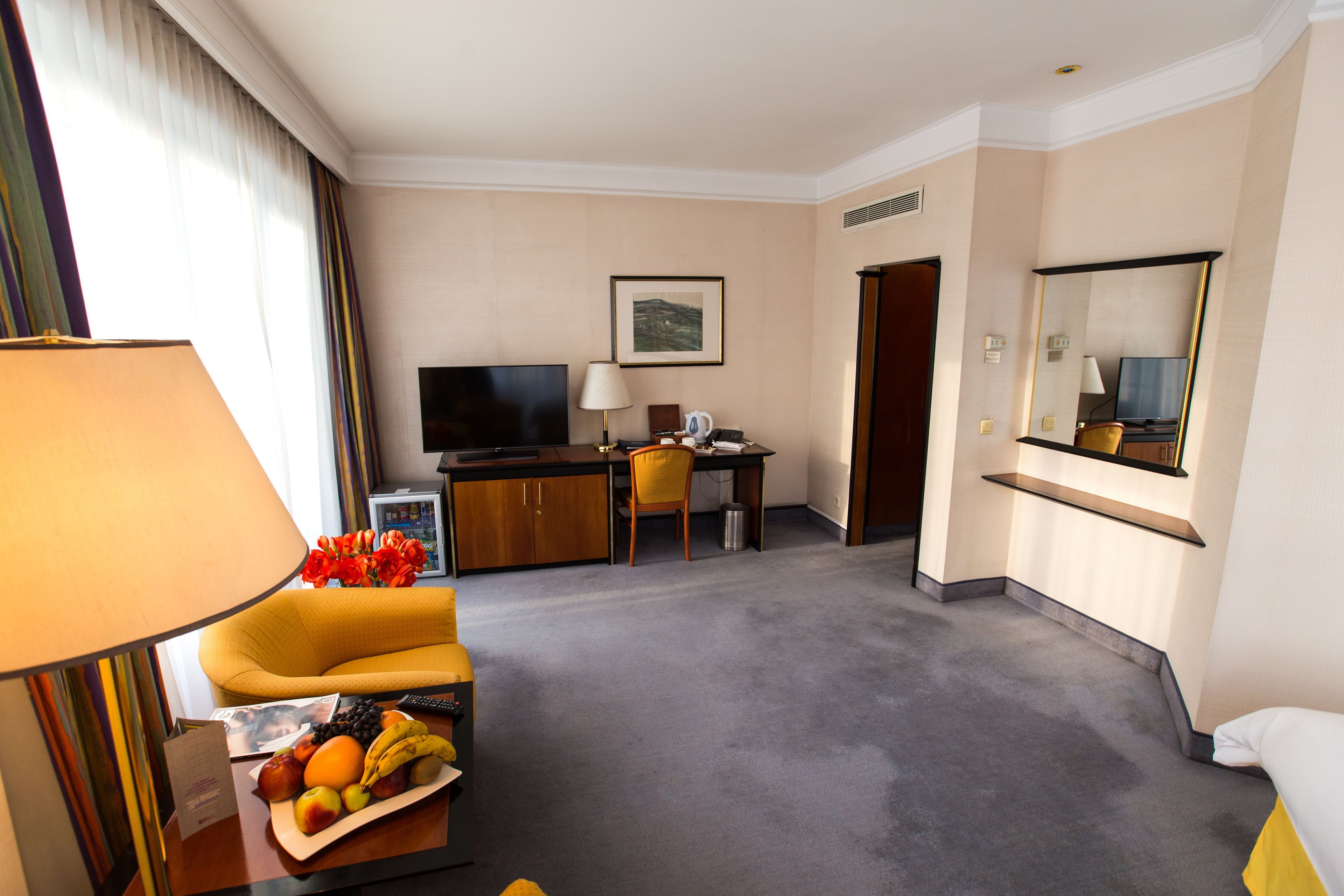 A hotel room with a sofa, a desk, a television, a mirror, and a fruit basket.