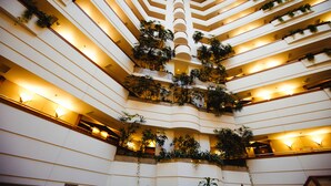 A multi-level atrium with balconies adorned with plants, a central staircase, and multiple floors with lighting. - Rahat Palace Hotel (Almaty)