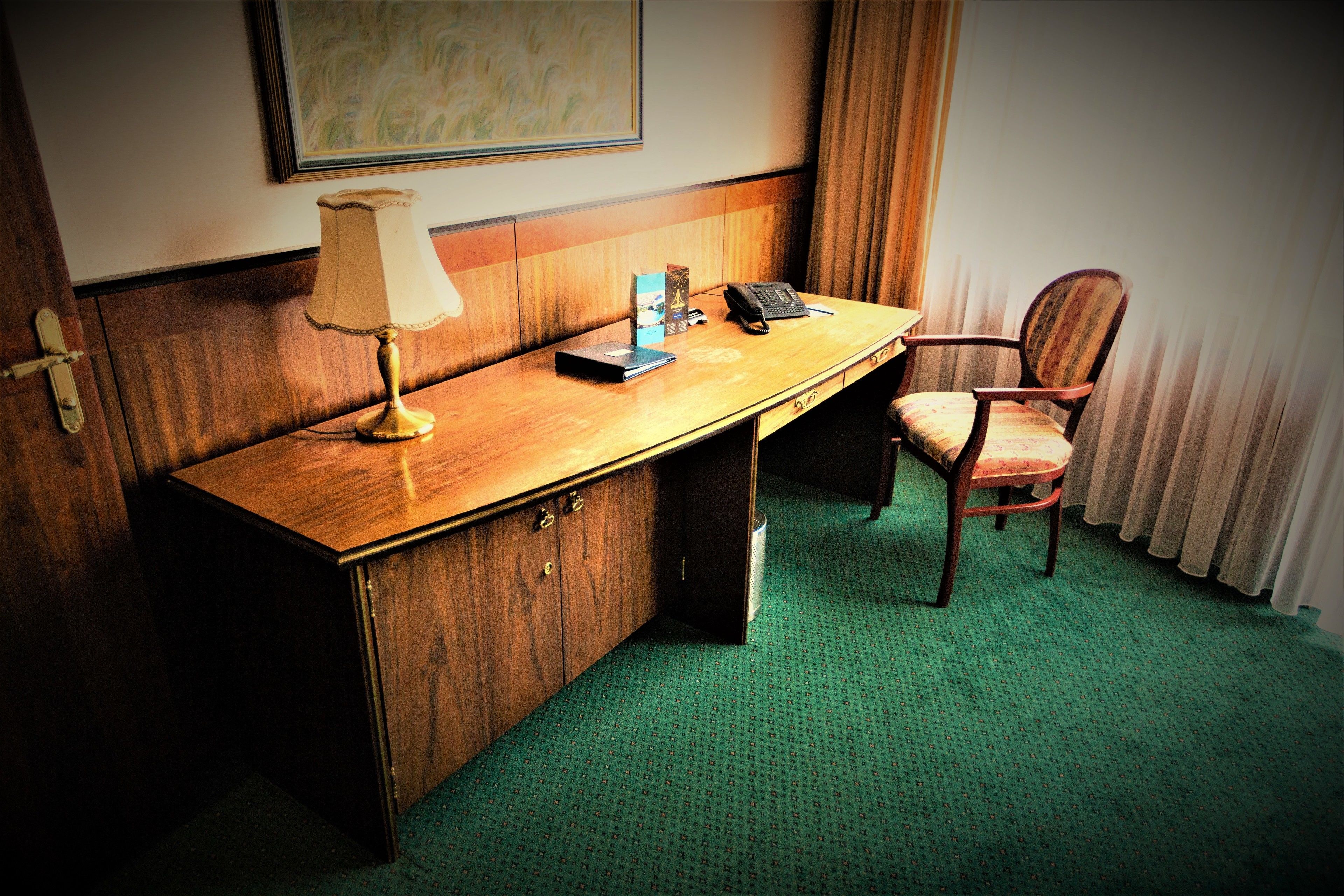 Habitación de hotel con un escritorio de madera, una lámpara, una silla y un cuadro en la pared.
