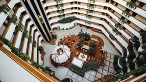 A multi-level atrium with a central circular seating area, multiple balconies with plants, and a modern architectural design. - Rahat Palace Hotel (Almaty)