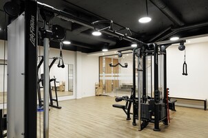 Un gimnasio con diverso equipo de ejercicio, suelo de madera y ventanas amplias.