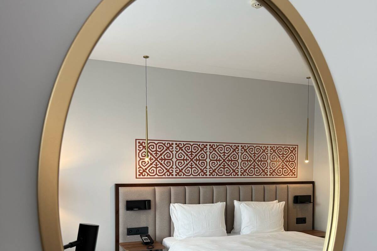A hotel room with a large bed, a desk, a chair, and a decorative wall panel.